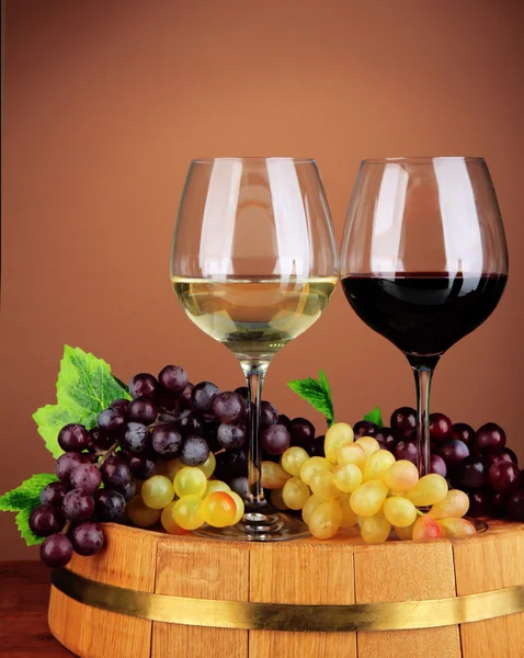 Glasses of red and white wine, grape on wooden barrel, on color background — Stock Photo, Image