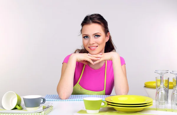 Schöne junge Frau wischt saubere Utensilien in der Küche auf grauem Hintergrund — Stockfoto