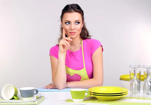 Beautiful young woman wipes clean utensils in kitchen on grey background — Stock Photo, Image