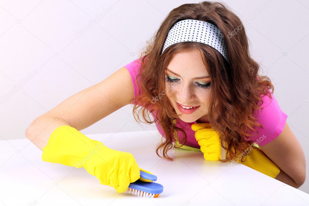Young housewife cleaning up table at home on grey background
