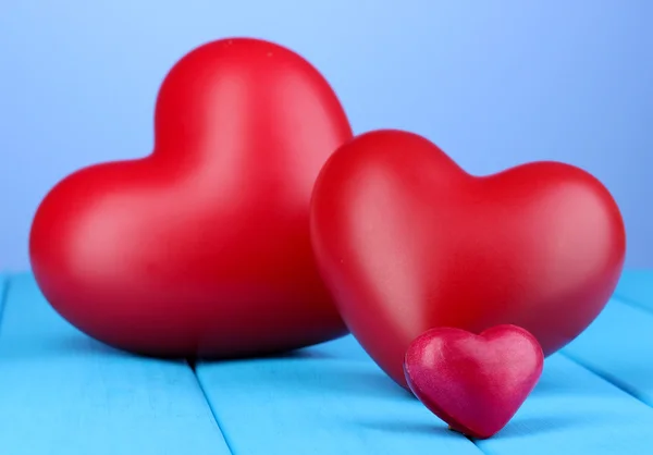 Corazones rojos decorativos sobre mesa de madera azul sobre fondo azul — Foto de Stock