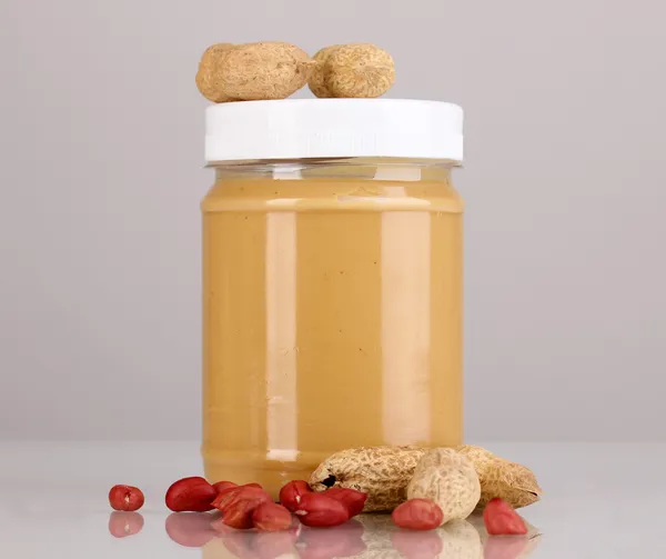 Смачне арахісове масло в банці з арахісом поблизу сірого фону — стокове фото