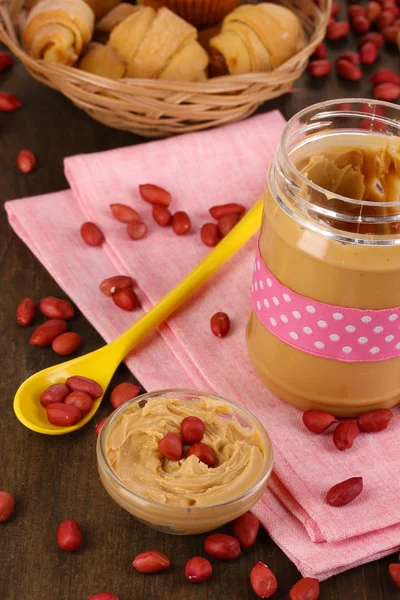 Delicious peanut butter in jar with baking on napkin on wooden table close-up — Stock Photo, Image