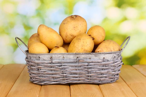 Ripe potatoes on basket on wooden table on natural background — Stock Photo, Image
