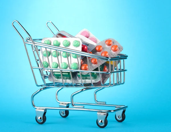 Shopping trolley with pills, on blue background — Stock Photo, Image