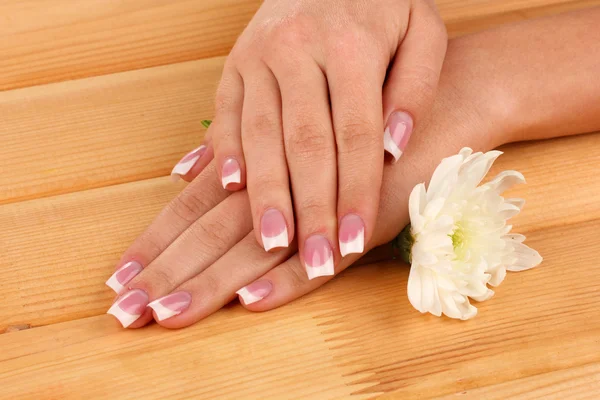 Vrouw handen met Frans manicure en bloem op houten achtergrond — Stockfoto