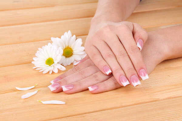 Woman hands with french manicure and flowers on wooden background