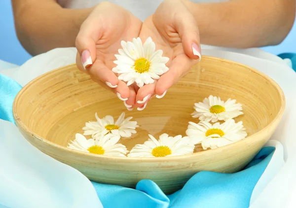 Manos de mujer con cuenco de madera de agua con flores, sobre fondo azul — Foto de Stock