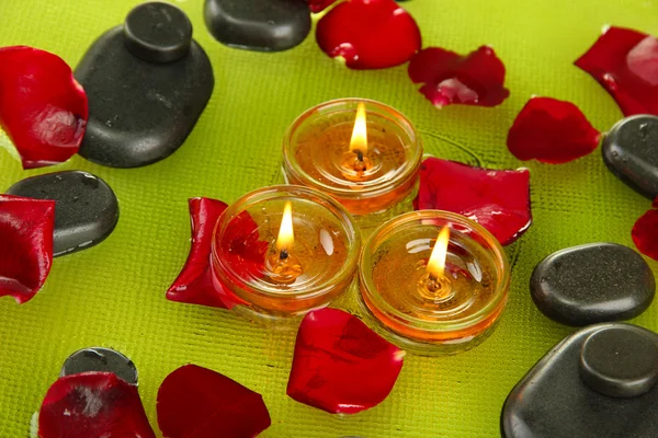 Spa stones with rose petals and candles in water on plate — Stock Photo, Image