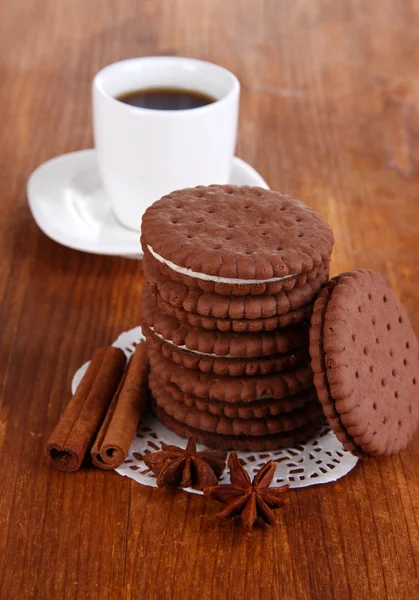 Chocolate cookies with creamy layer and cup of coffe on wooden table close-up — Stock Photo, Image