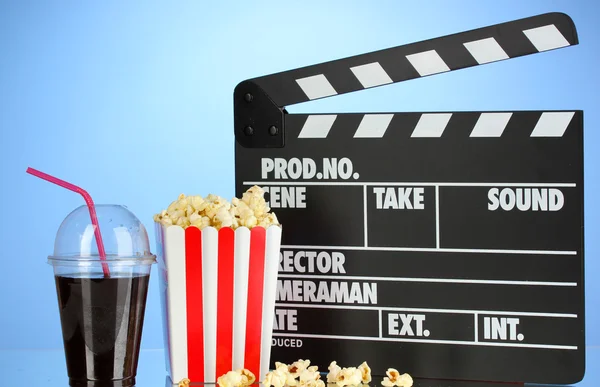 Movie clapperboard, cola and popcorn on blue background — Stock Photo, Image