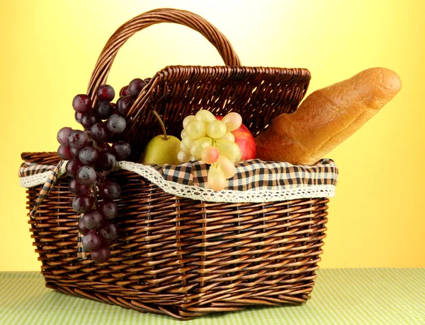 Piknik sepeti meyve üzerinde sarı zemin üzerine bir bez ile — Stok fotoğraf