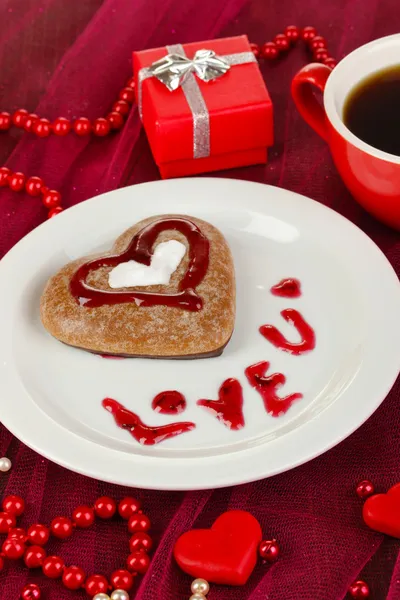 Chocolate cookie in form of heart with cup of coffee on pink tablecloth close-up — Stock Photo, Image