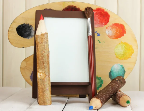 Photo frame as easel with artist's tools on wooden background — Stock Photo, Image