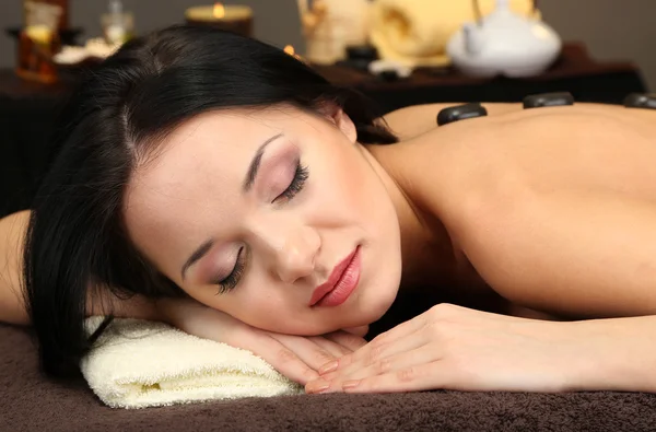 Hermosa joven en el salón de spa con piedras de spa, sobre fondo oscuro — Foto de Stock