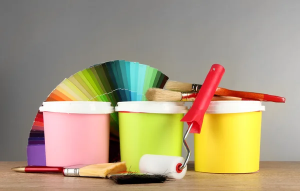 Farbtöpfe, Pinsel und Farbmuster auf Holztisch auf grauem Hintergrund — Stockfoto