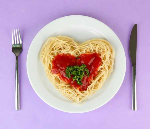 Готовые спагетти тщательно расположены в форме сердца и увенчаны томатным соусом, на цветном фоне — стоковое фото