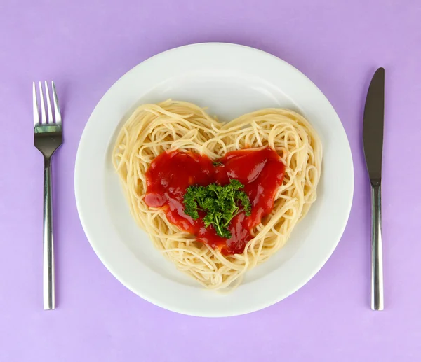 Cooked spaghetti carefully arranged in heart shape and topped with tomato sauce, on color background