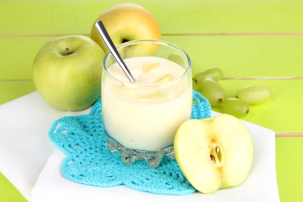 Glass of yogurt with apples and grape on napkin on wooden background — Stock Photo, Image