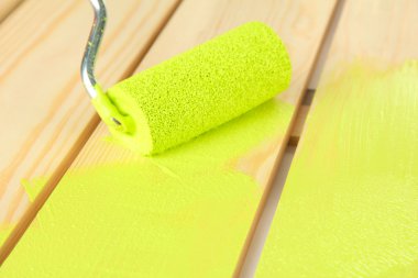 Paint roller brush with green paint, on wooden background clipart