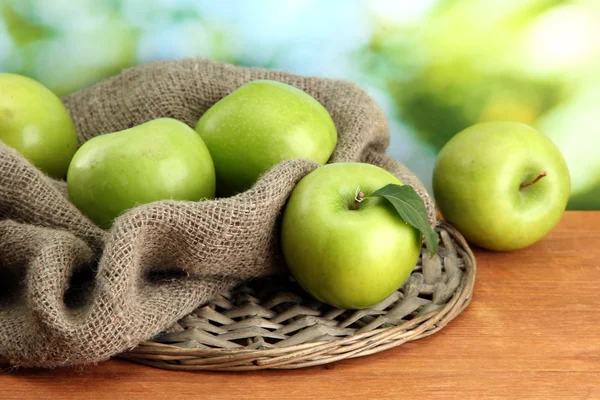 Ripe green apples with leaves on burlap, on wooden table, on green background — Stock Photo, Image