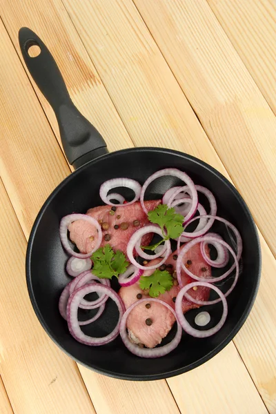 Ein Stück Schweinefleisch mit Zwiebeln in Pfanne auf Holztisch gebraten — Stockfoto