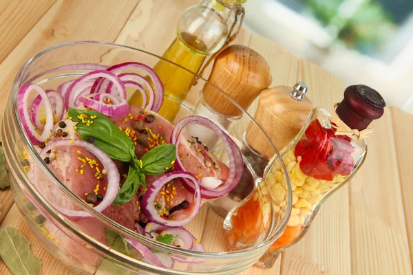 A large piece of pork marinated in bowl with herbs, spices and cooking oil close-up on wooden table on window background — Stock Photo, Image