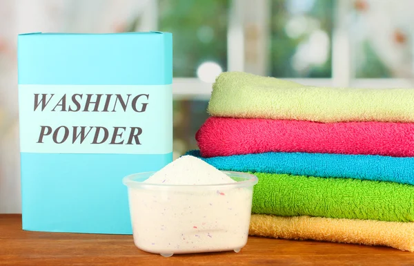 Box of washing powder with blue measuring cup and towels, on wooden table close-up — Stock Photo, Image