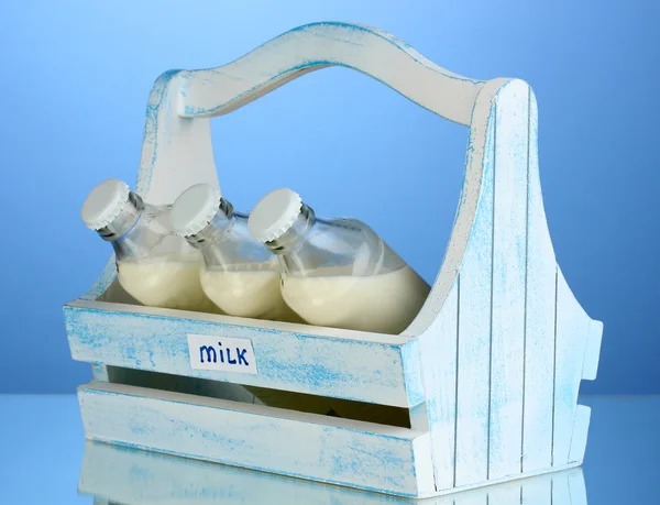 Milk in bottles in wooden box on blue background — Stock Photo, Image