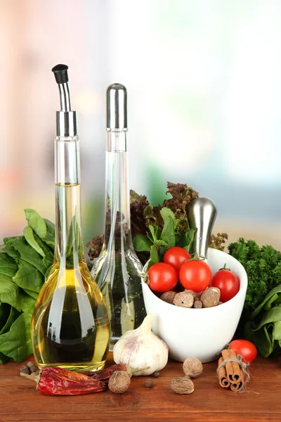 Composition of mortar, bottles with olive oil and vinegar, and green herbals, on bright background — Stock Photo, Image