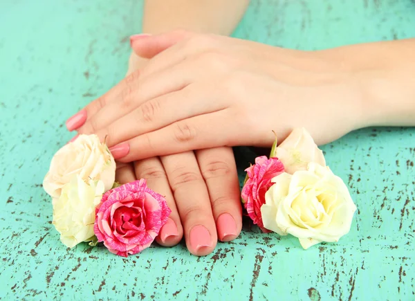 Mãos de mulher com manicure rosa e flores, em fundo de cor — Fotografia de Stock