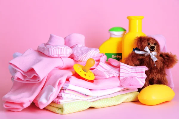 Pilha de roupas de bebê no fundo rosa — Fotografia de Stock