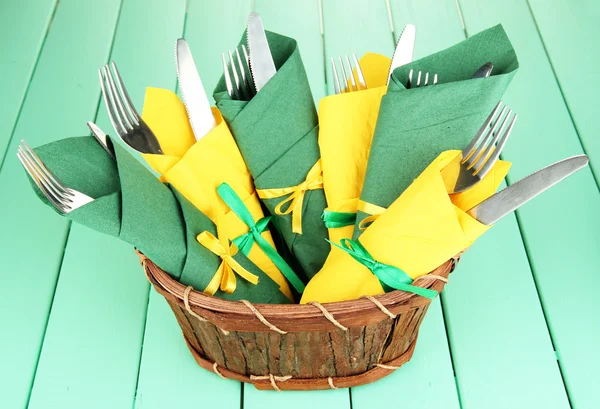 Tenedores y cuchillos envueltos en servilletas de papel verde y amarillo, sobre fondo de madera de color —  Fotos de Stock