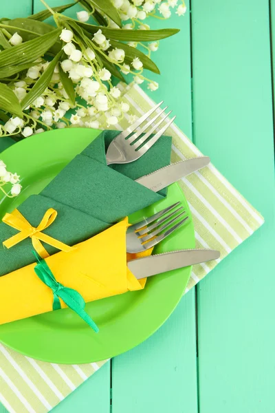 Tenedores y cuchillos envueltos en servilletas de papel verde y amarillo, sobre fondo de madera de color —  Fotos de Stock