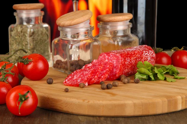 Smakelijke salami aan boord van houten tafel op brand achtergrond — Stockfoto