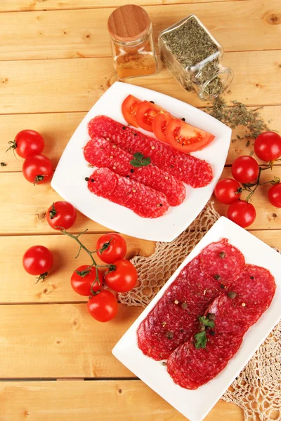 Tasty salami on plates on wooden table close-up — Stock Photo, Image