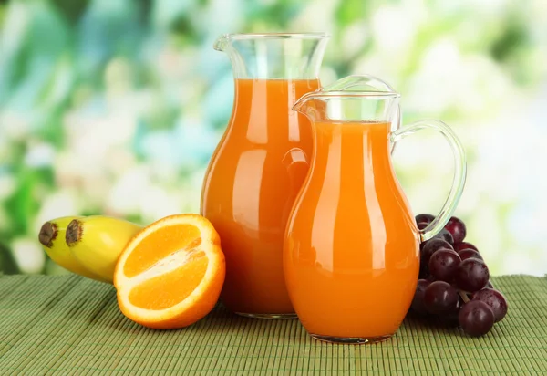 Sumo de laranja em jarros na mesa sobre fundo brilhante — Fotografia de Stock