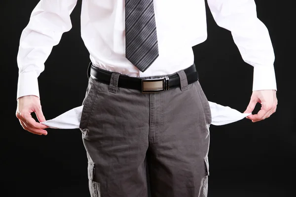 Geschäftsmann zeigt seine leeren Taschen auf schwarzem Hintergrund — Stockfoto