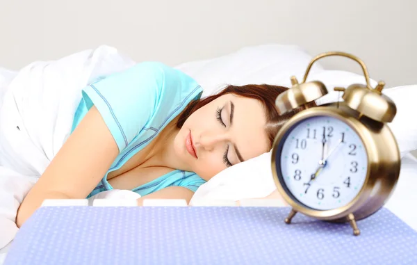 Beautiful young woman sleeping on bed with alarm clock in bedroom — Stock Photo, Image