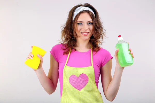 Young housewife with cleaner and sponge on grey background — Stock Photo, Image