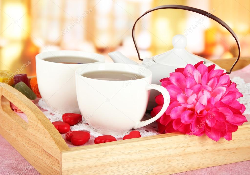 Cups of tea with flower and teapot on wooden tray on table in cafe