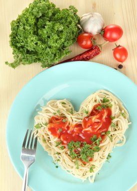 Cooked spaghetti carefully arranged in heart shape and topped with tomato sauce, on wooden background