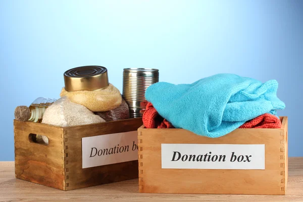 Donation boxes with clothing and food on blue background close-up — Stock Photo, Image