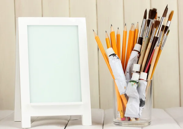 Photo frame as easel with artist's tools on wooden background — Stock Photo, Image