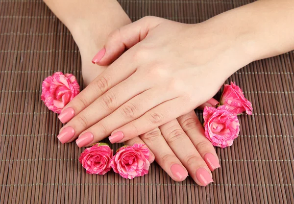 Mãos de mulher com manicure rosa e flores, em fundo tapete de bambu — Fotografia de Stock