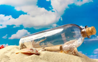 Glass bottle with note inside on sand, on blue sky background clipart