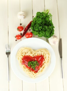 Cooked spaghetti carefully arranged in heart shape and topped with tomato sauce, on wooden background