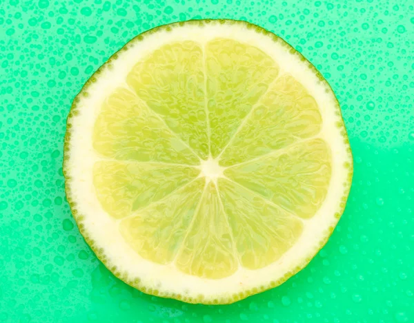 Slice of lime with drop on green background — Stock Photo, Image