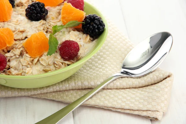 Flocons d'avoine savoureux aux baies et fruits, sur table en bois blanc — Photo