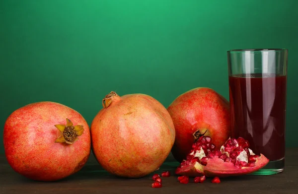 Ripe pomegranates with glass of pomegranate juice on green background — Stock Photo, Image